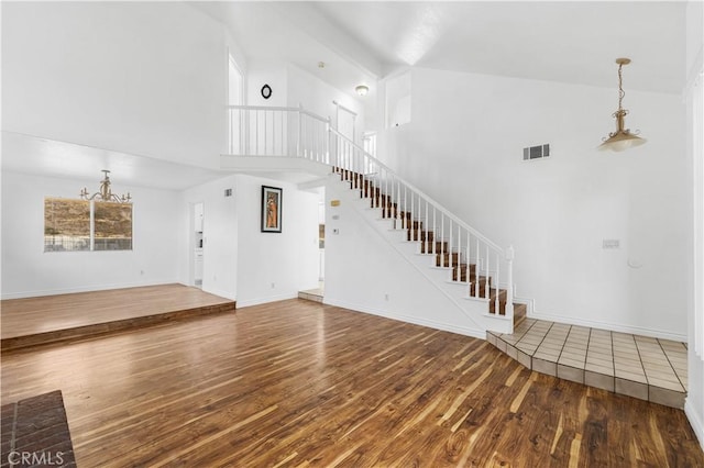 unfurnished living room with high vaulted ceiling, hardwood / wood-style floors, and a chandelier