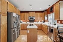 kitchen with appliances with stainless steel finishes, sink, light hardwood / wood-style floors, and a kitchen island