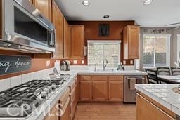 kitchen featuring light wood-type flooring, stainless steel appliances, tile countertops, and sink