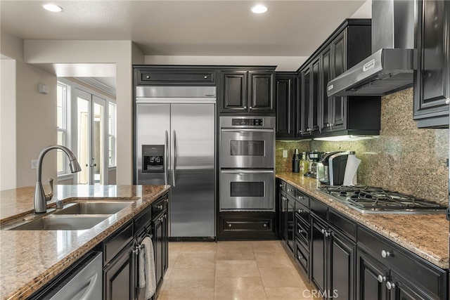 kitchen featuring light stone countertops, appliances with stainless steel finishes, wall chimney exhaust hood, sink, and light tile patterned floors