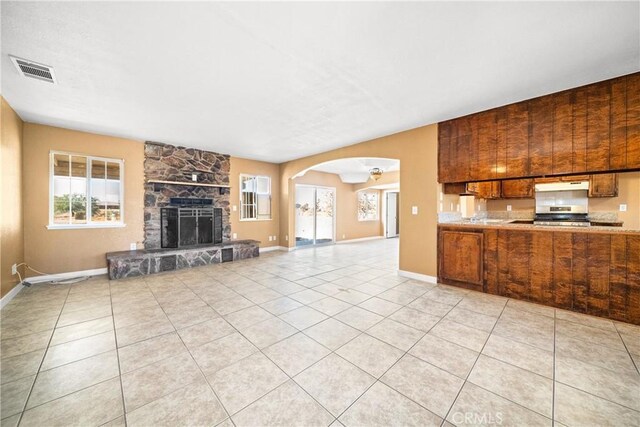 unfurnished living room with ceiling fan, light tile patterned floors, and a stone fireplace