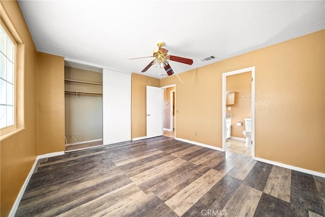 unfurnished bedroom featuring ceiling fan, multiple windows, hardwood / wood-style floors, and ensuite bath