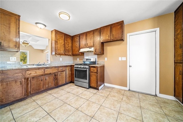 kitchen featuring light tile patterned floors, stainless steel gas range oven, sink, and light stone counters