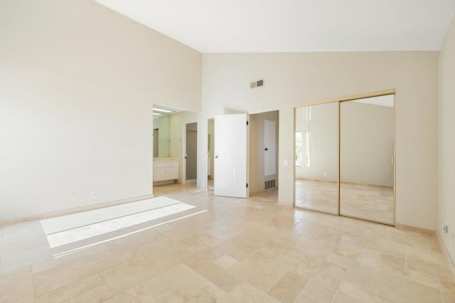 unfurnished bedroom featuring high vaulted ceiling, ensuite bath, and a closet