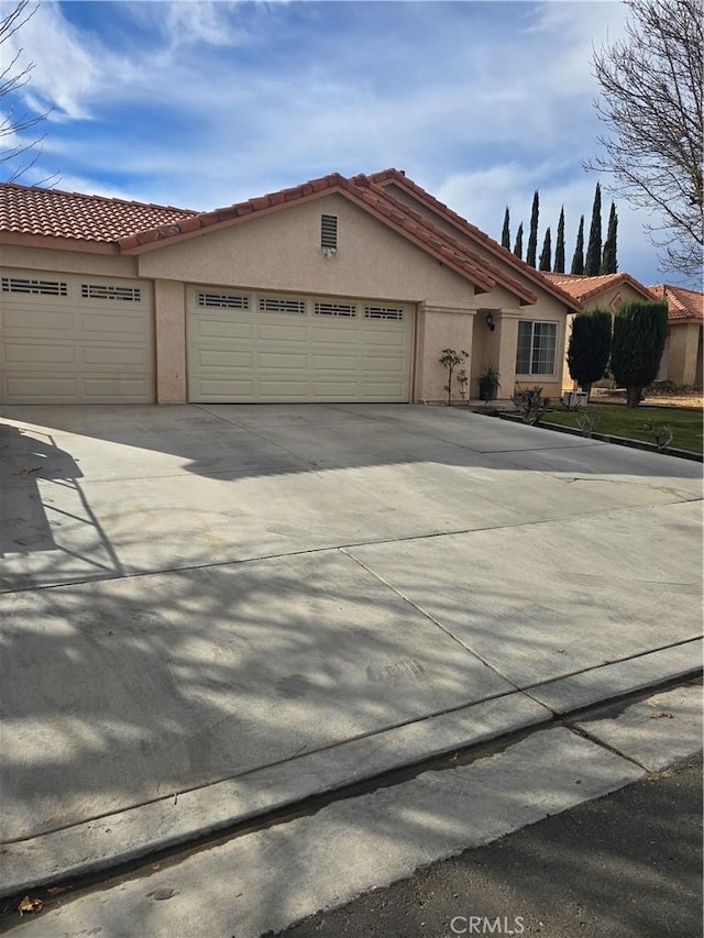 view of front of house with driveway, a tiled roof, an attached garage, and stucco siding