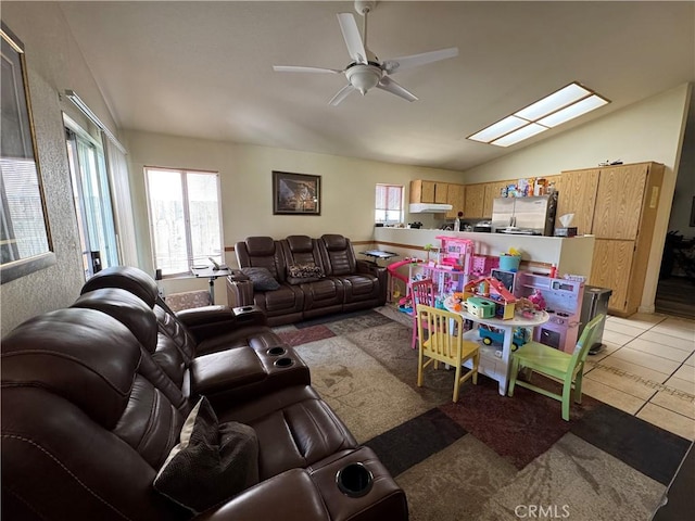 living room featuring a ceiling fan, vaulted ceiling with skylight, and light tile patterned flooring