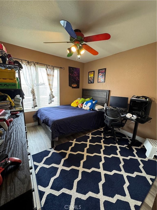 bedroom with baseboards, a textured ceiling, a ceiling fan, and wood finished floors