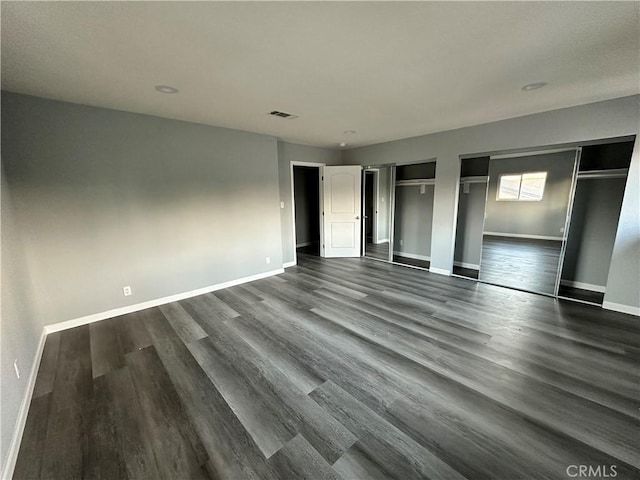 unfurnished bedroom with two closets and dark hardwood / wood-style flooring