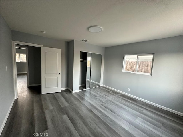 unfurnished bedroom with a closet, dark hardwood / wood-style floors, and multiple windows