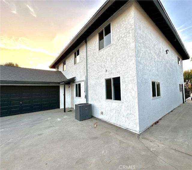 property exterior at dusk with central AC unit and a garage