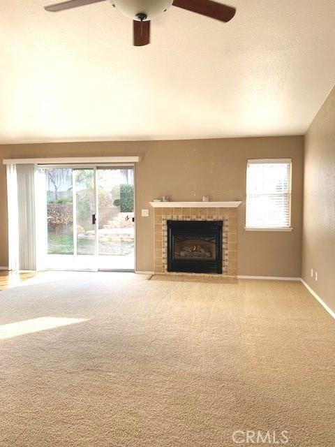 unfurnished living room with ceiling fan, light colored carpet, and a tile fireplace