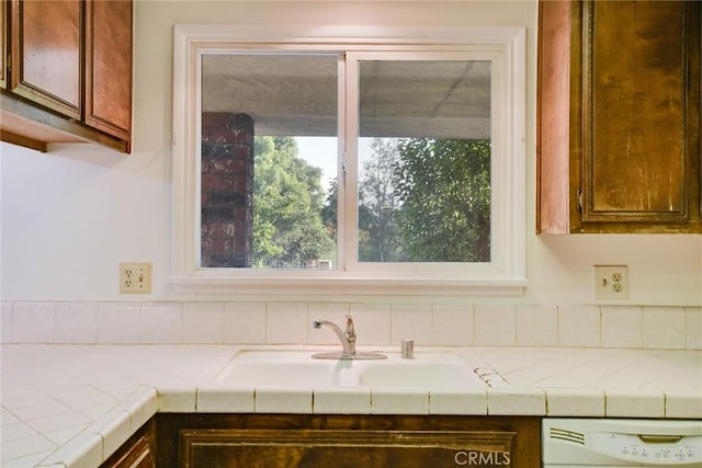 kitchen featuring white dishwasher, sink, and tile counters