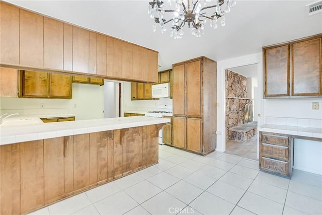 kitchen featuring a notable chandelier, tile countertops, sink, light tile patterned floors, and range