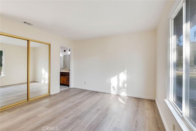 unfurnished bedroom with a closet, light hardwood / wood-style floors, and ensuite bath