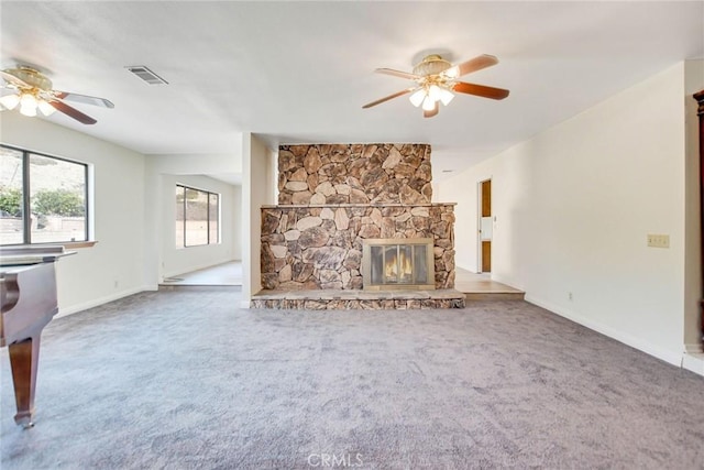 unfurnished living room featuring ceiling fan, a stone fireplace, and carpet flooring