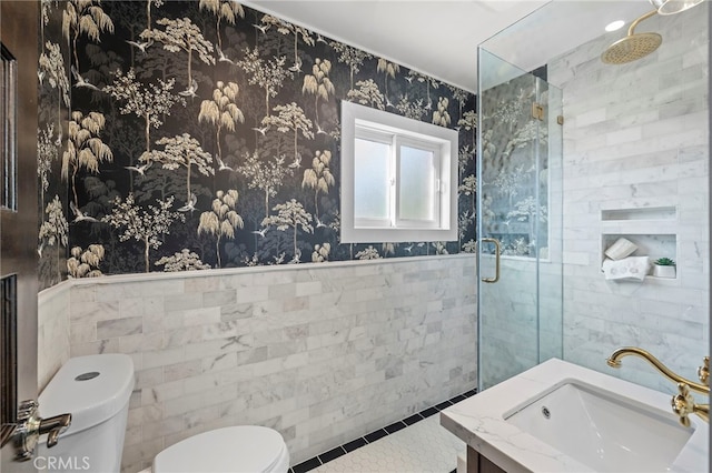 bathroom featuring toilet, vanity, tile walls, tile patterned floors, and a shower with door