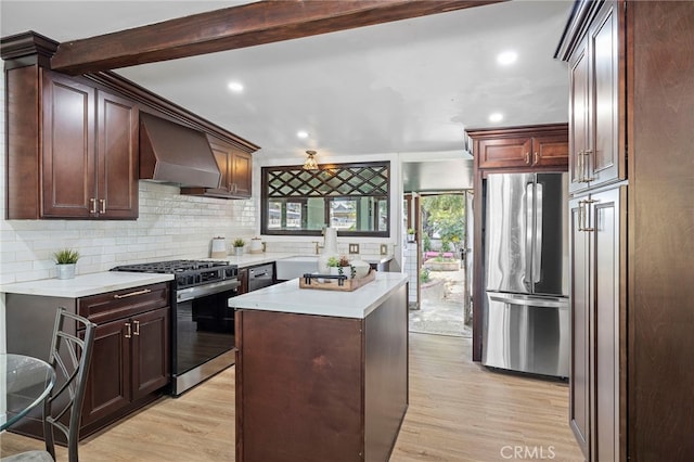 kitchen with appliances with stainless steel finishes, a center island, custom exhaust hood, beamed ceiling, and light wood-type flooring