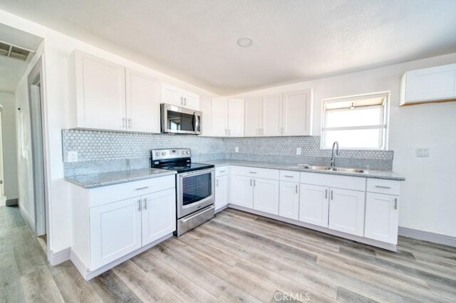 kitchen with sink, light hardwood / wood-style flooring, light stone countertops, stainless steel appliances, and white cabinets