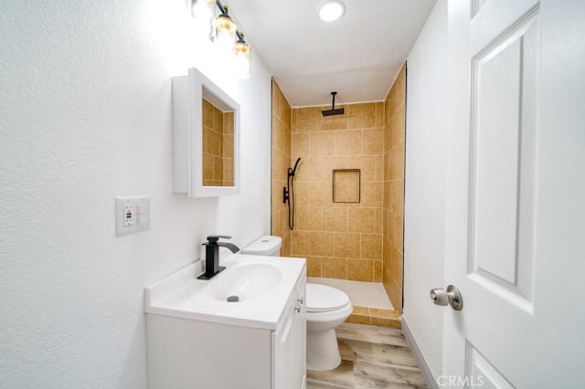 bathroom with hardwood / wood-style floors, toilet, vanity, and a tile shower