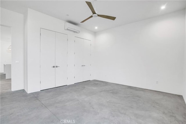 unfurnished bedroom featuring ceiling fan, an AC wall unit, multiple closets, and concrete flooring