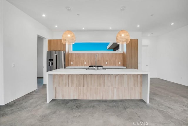 kitchen with decorative light fixtures, a kitchen island with sink, sink, and high end refrigerator