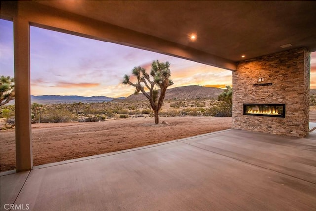 patio terrace at dusk featuring a mountain view and an outdoor stone fireplace