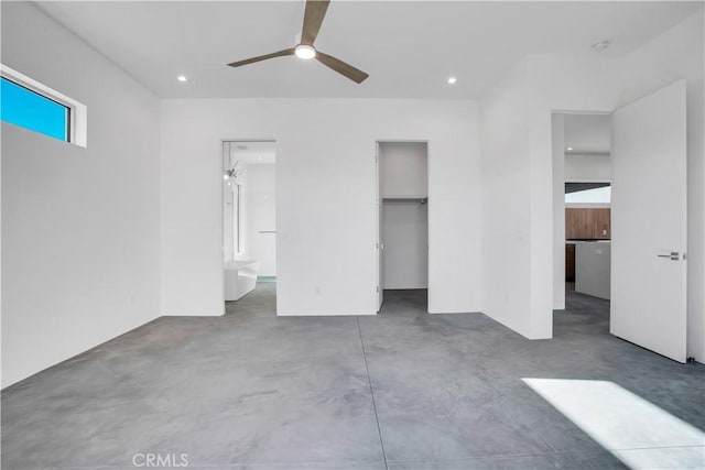 unfurnished bedroom featuring ensuite bathroom, ceiling fan, concrete floors, a walk in closet, and a closet