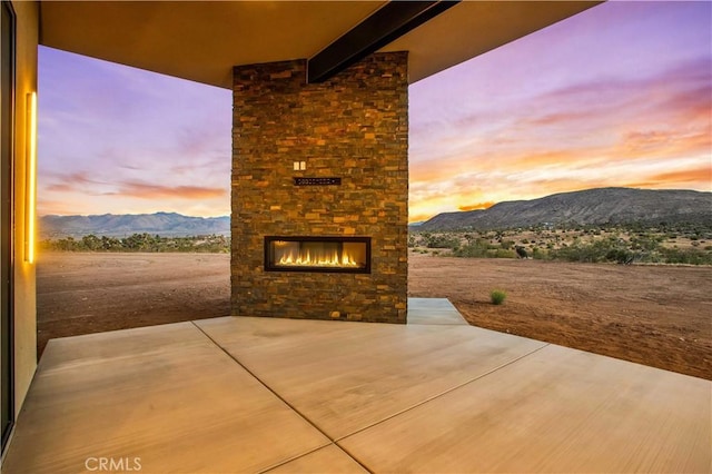 patio terrace at dusk with an outdoor stone fireplace and a mountain view