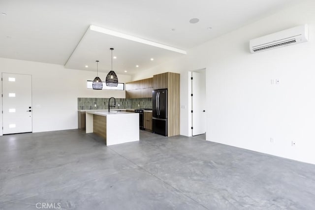 kitchen with an AC wall unit, black appliances, decorative light fixtures, sink, and a kitchen island with sink