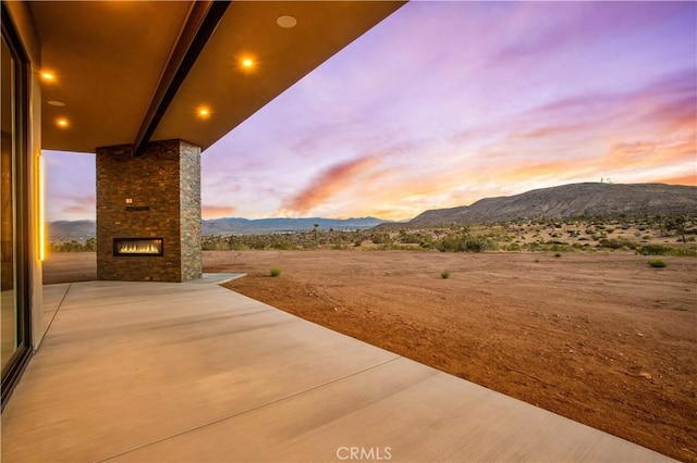 patio terrace at dusk featuring a mountain view and exterior fireplace