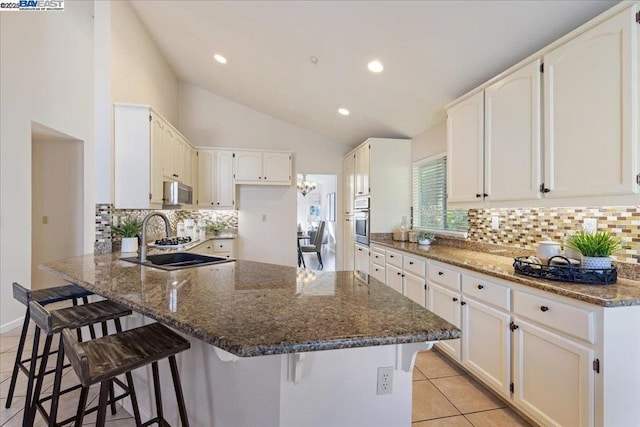 kitchen featuring sink, white cabinetry, appliances with stainless steel finishes, a kitchen breakfast bar, and dark stone counters