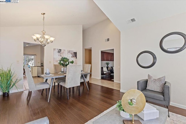 dining area featuring a notable chandelier, wood-type flooring, and high vaulted ceiling