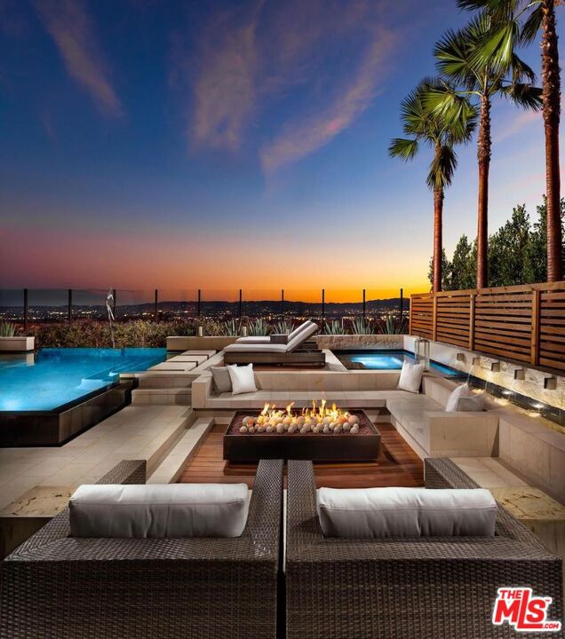 pool at dusk featuring pool water feature, an outdoor living space with a fire pit, and a patio