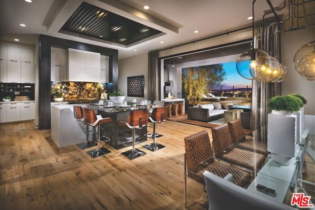 kitchen featuring white cabinets, a kitchen island, tasteful backsplash, light wood-type flooring, and a breakfast bar