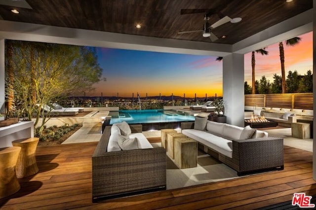 deck at dusk with ceiling fan and an outdoor living space with a fire pit