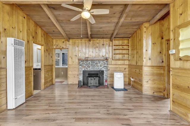 unfurnished living room with wood walls, a wood stove, beam ceiling, and wood ceiling