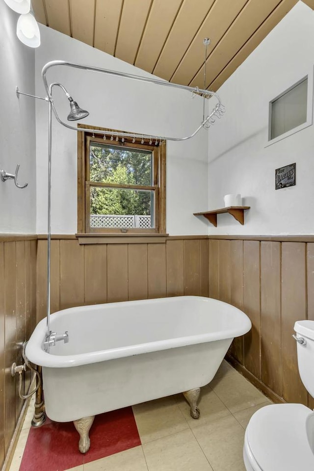 bathroom featuring wood ceiling, tile patterned floors, wooden walls, toilet, and a washtub