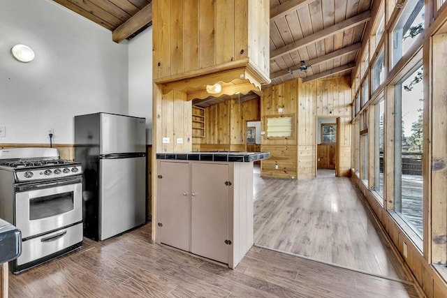 kitchen featuring tile counters, stainless steel appliances, beamed ceiling, wooden walls, and hardwood / wood-style flooring