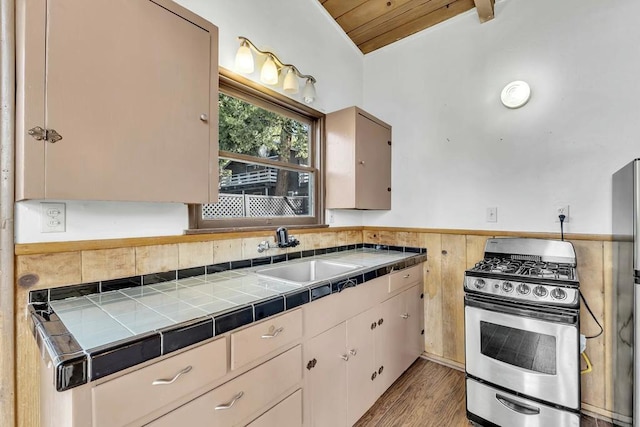 kitchen with light hardwood / wood-style floors, lofted ceiling with beams, sink, appliances with stainless steel finishes, and tile counters