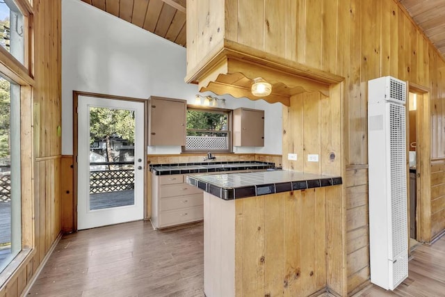 kitchen featuring hardwood / wood-style flooring, tile countertops, wood walls, and high vaulted ceiling