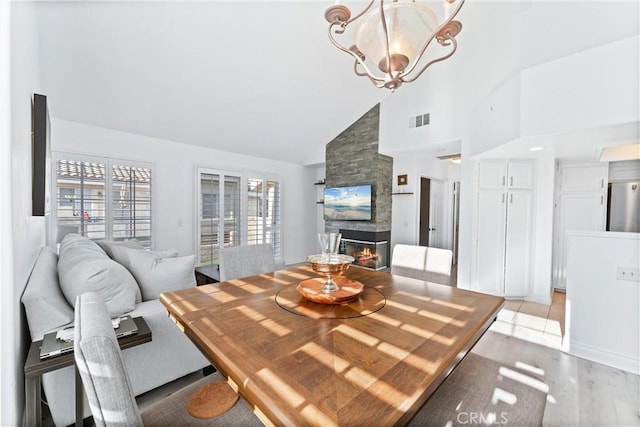 dining room with light wood-type flooring, an inviting chandelier, a fireplace, and high vaulted ceiling