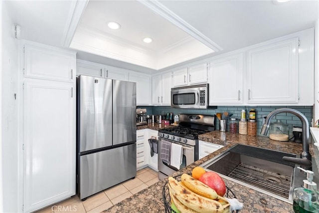 kitchen with white cabinets, appliances with stainless steel finishes, sink, light tile patterned floors, and a tray ceiling