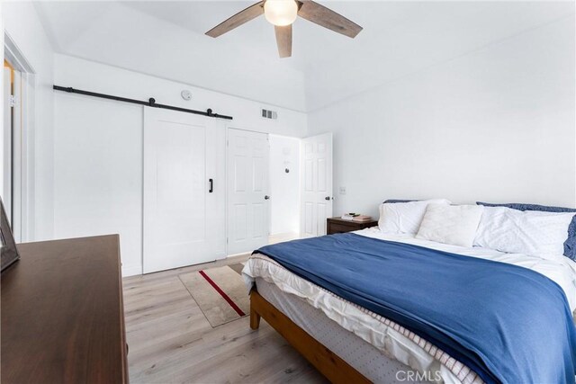 bedroom with ceiling fan, light hardwood / wood-style flooring, a closet, and a barn door