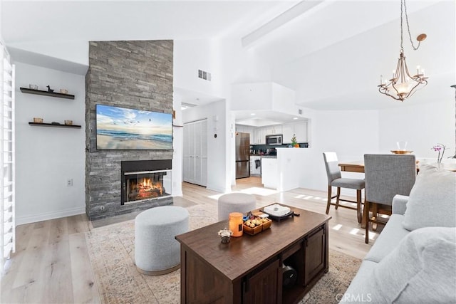 living room featuring light wood-type flooring, lofted ceiling with beams, an inviting chandelier, and a stone fireplace