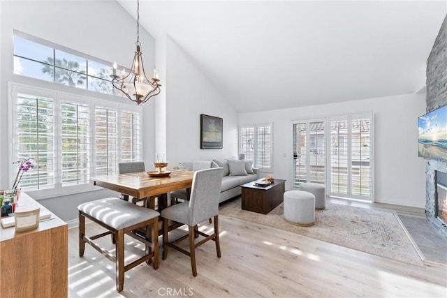 dining space featuring high vaulted ceiling, light wood-type flooring, a fireplace, and an inviting chandelier