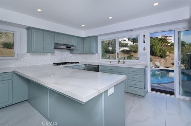 kitchen featuring marble finish floor, backsplash, a sink, a peninsula, and under cabinet range hood