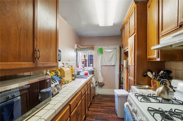 kitchen with tile countertops, tasteful backsplash, dark wood-type flooring, white gas range oven, and sink