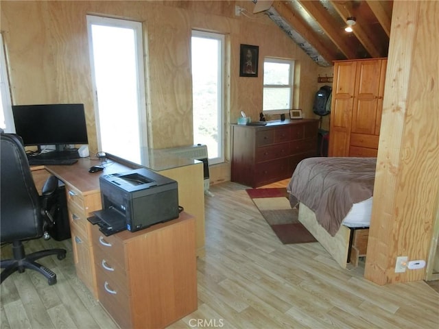 bedroom with vaulted ceiling, wooden walls, light wood-type flooring, and multiple windows