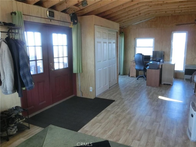 foyer with vaulted ceiling, light hardwood / wood-style floors, wooden walls, heating unit, and french doors