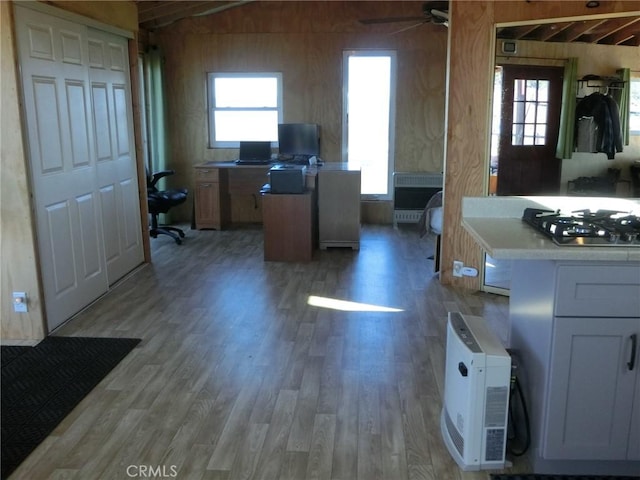 kitchen featuring white cabinetry, wood walls, light wood-type flooring, ceiling fan, and stainless steel gas stovetop